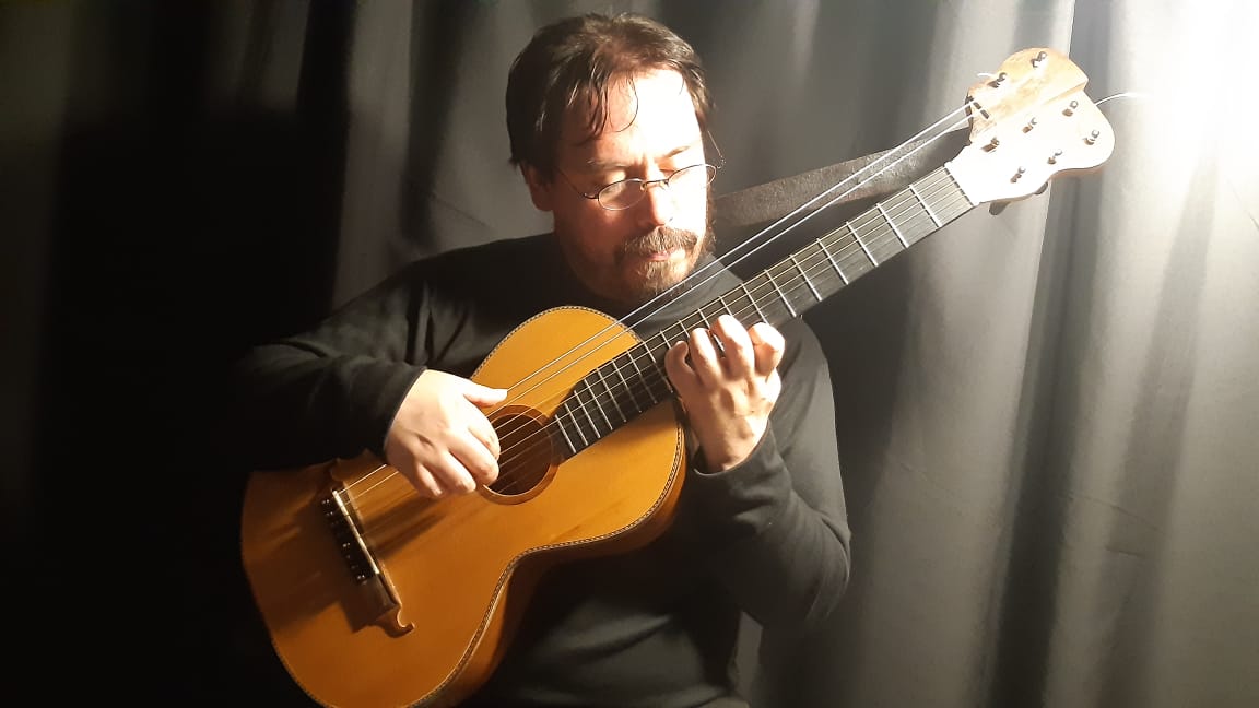 Andrés Zapico tocando su guitarra romántica de ocho cuerdas con luz lateral sobre fondo oscuro